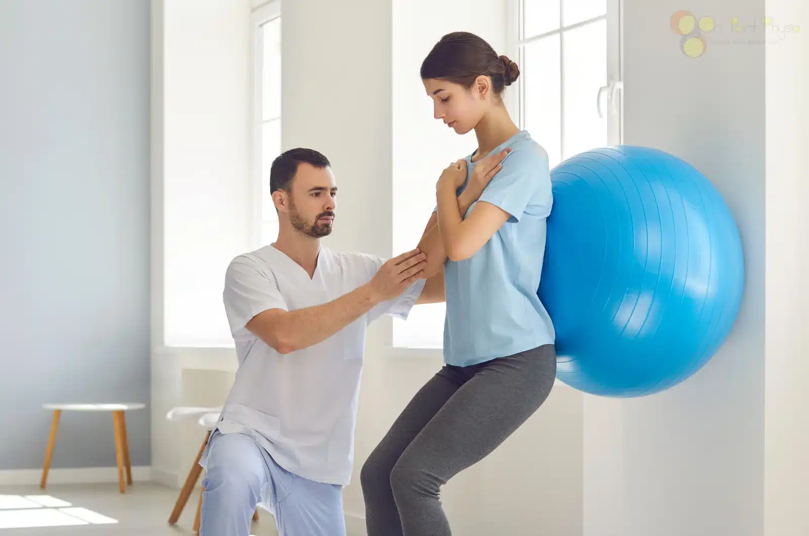 Woman doing ball-supported wall squats assisted by physiotherapist in clinic.